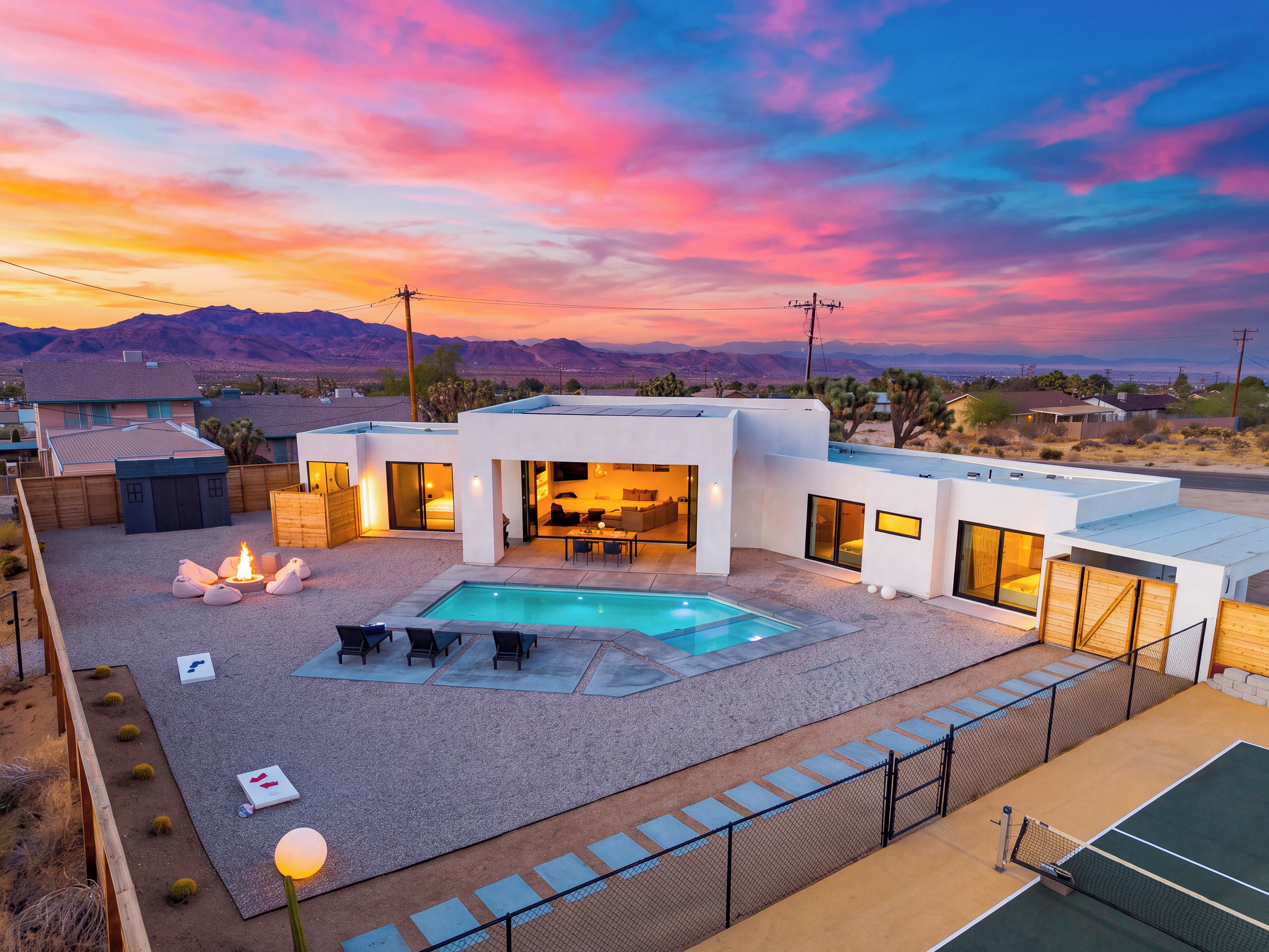 A modern house with a swimming pool, outdoor seating, and a tennis court.