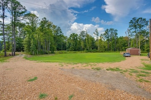A gravel driveway leading to a grassy area with a building and a car parked nearby.