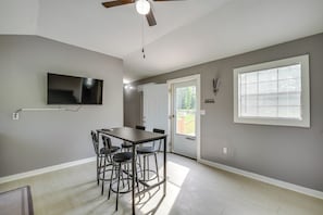 A dining area with a table and chairs, a ceiling fan, a mounted TV, and a window with blinds.