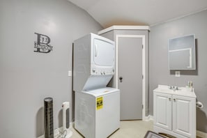 A laundry room with a stacked washer and dryer, a thermostat, and a sign indicating energy usage.