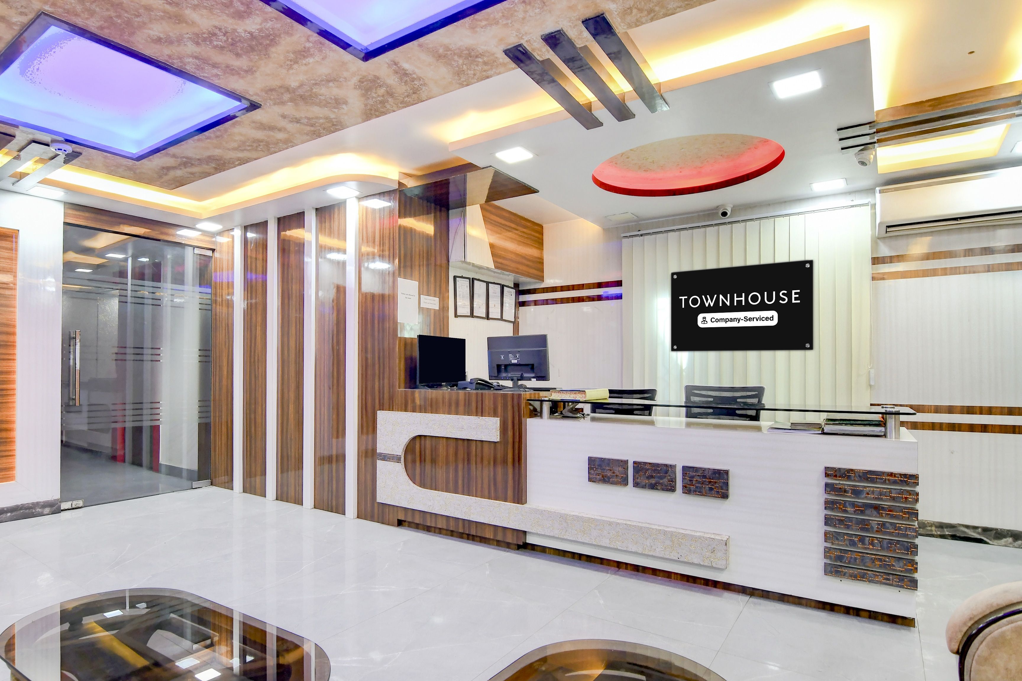 A reception area with a modern design, featuring a reception desk, a mounted TV, and a sign that reads 'TOWNHOUSE Company-Serviced'.
