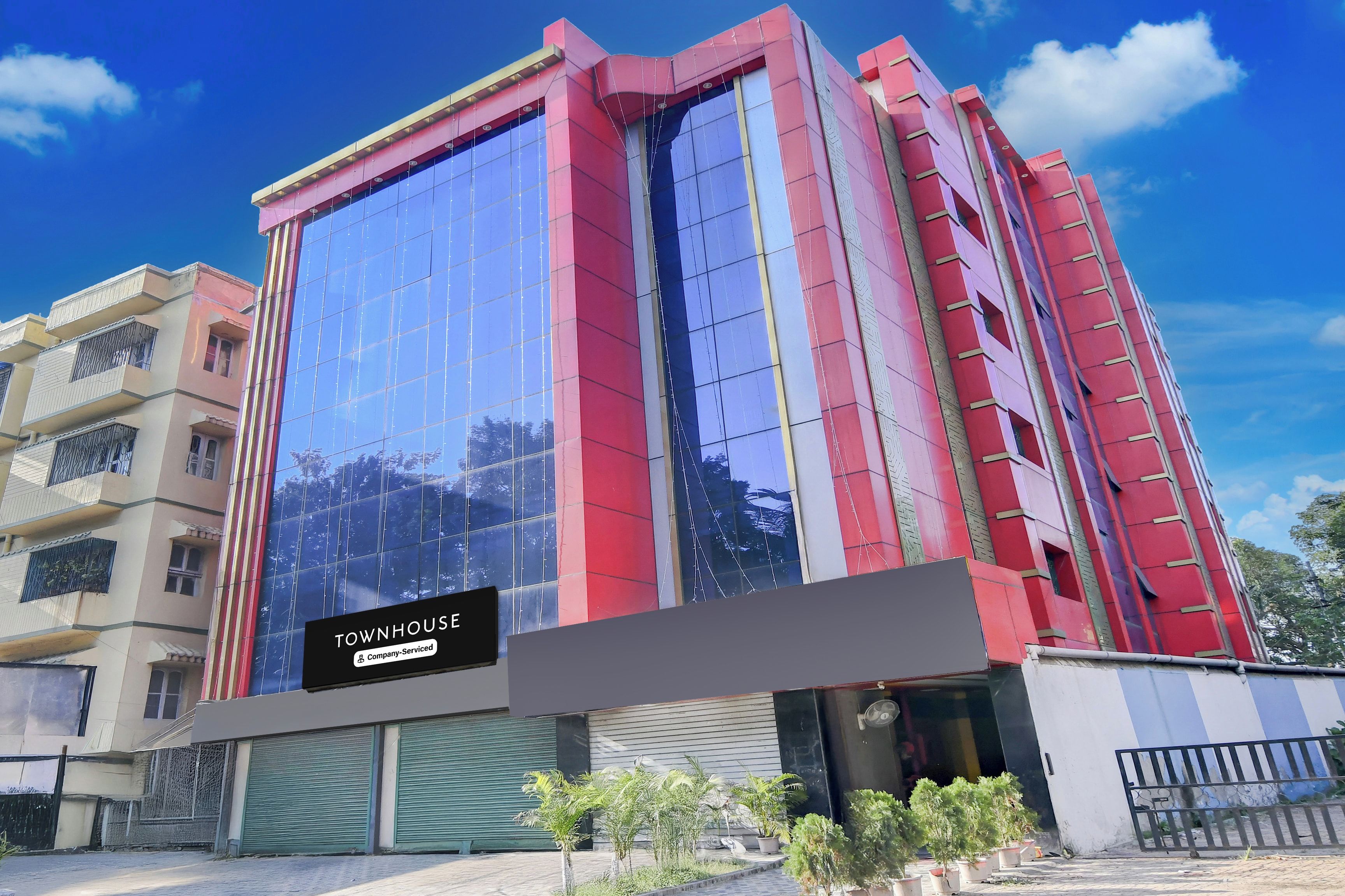 A multi-story building with a large glass facade, a sign indicating 'TOWNHOUSE Company Serviced,' and a gated entrance.
