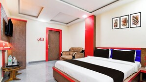 Quarto de hotel com uma cama, uma cadeira, uma mesinha com garrafas de água e uma parede com detalhes em vermelho.