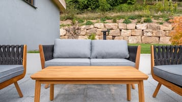 A patio with a grey sofa, two wooden chairs, and a wooden table.
