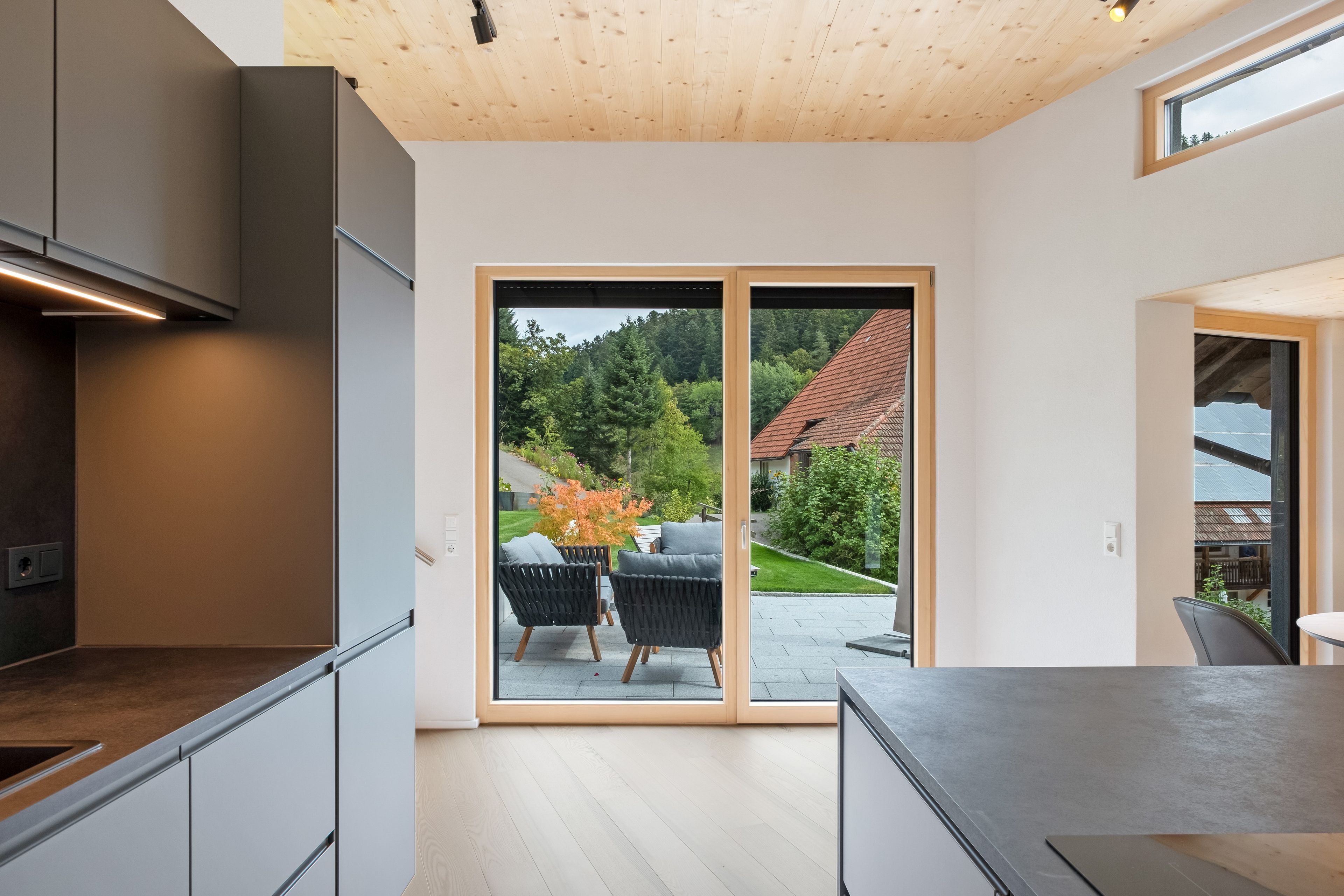 A modern kitchen with a sliding glass door leading to an outdoor seating area with two chairs.