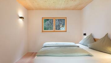 A bedroom with a wooden ceiling, a bed with pillows, a nightstand, and a window with a view of trees.