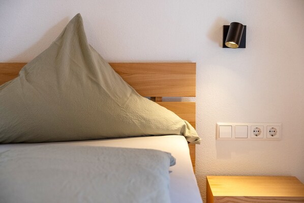 A bed with a wooden headboard, a pillow, a bedside table, and a wall-mounted light fixture.