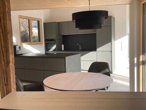 A modern kitchen with a central island, built-in appliances, and a round dining table. - Holiday Home 'Bienenhäusle' with Private Terrace and Garden (Gutach (Schwarzwaldbahn))