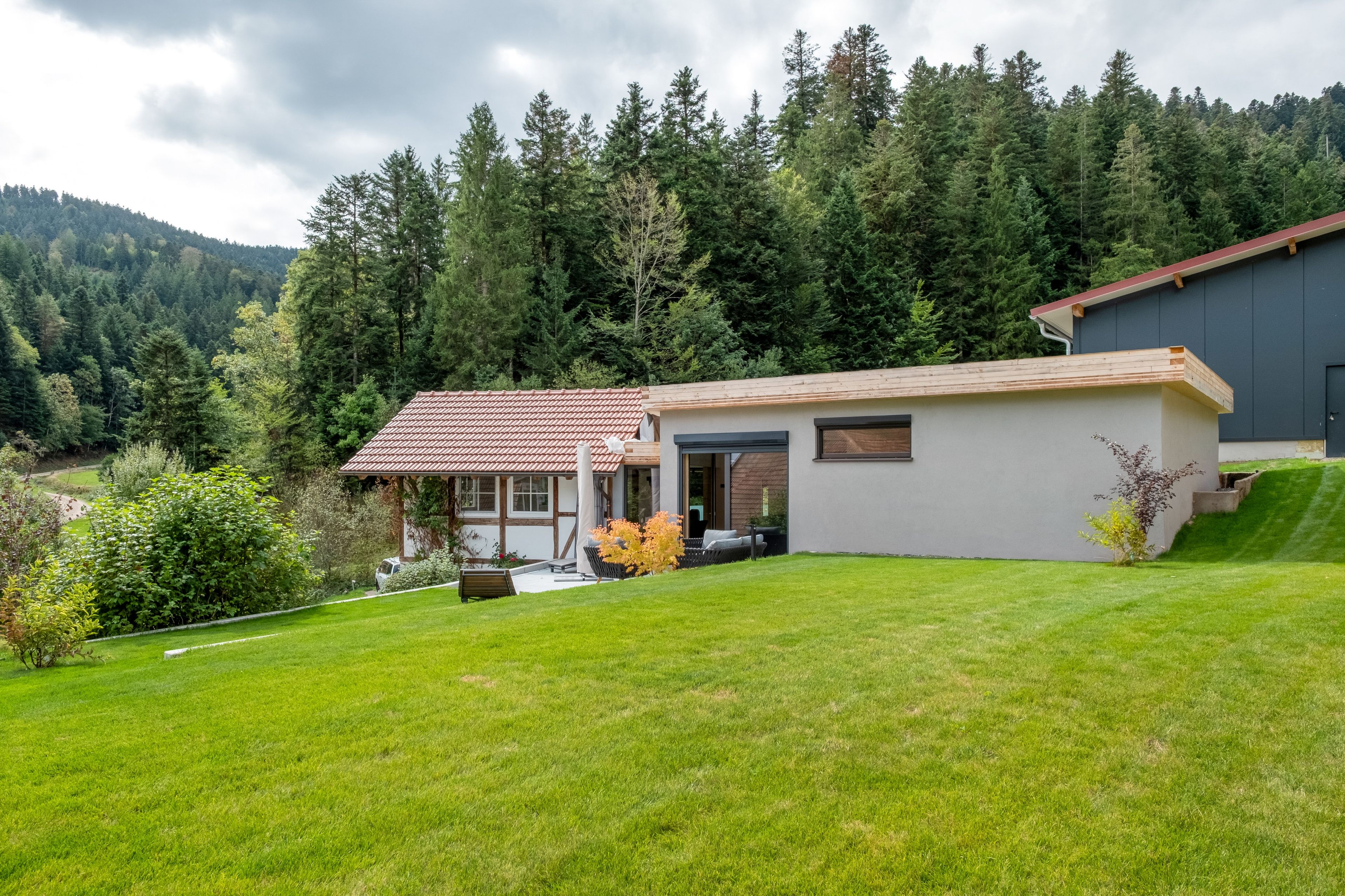 Une maison moderne avec un toit recouvert de tuiles rouges, une véranda et une pelouse bien entretenue.