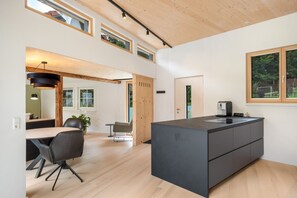A modern kitchen with a central island, wooden flooring, and a view of the outdoors through large windows.