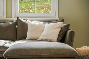 A sofa with two pillows and a window with a view of greenery.