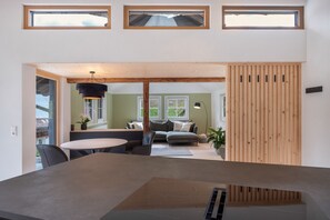 A modern interior with a dining area, a living room with a sofa and a table, and a kitchen visible through an open doorway.