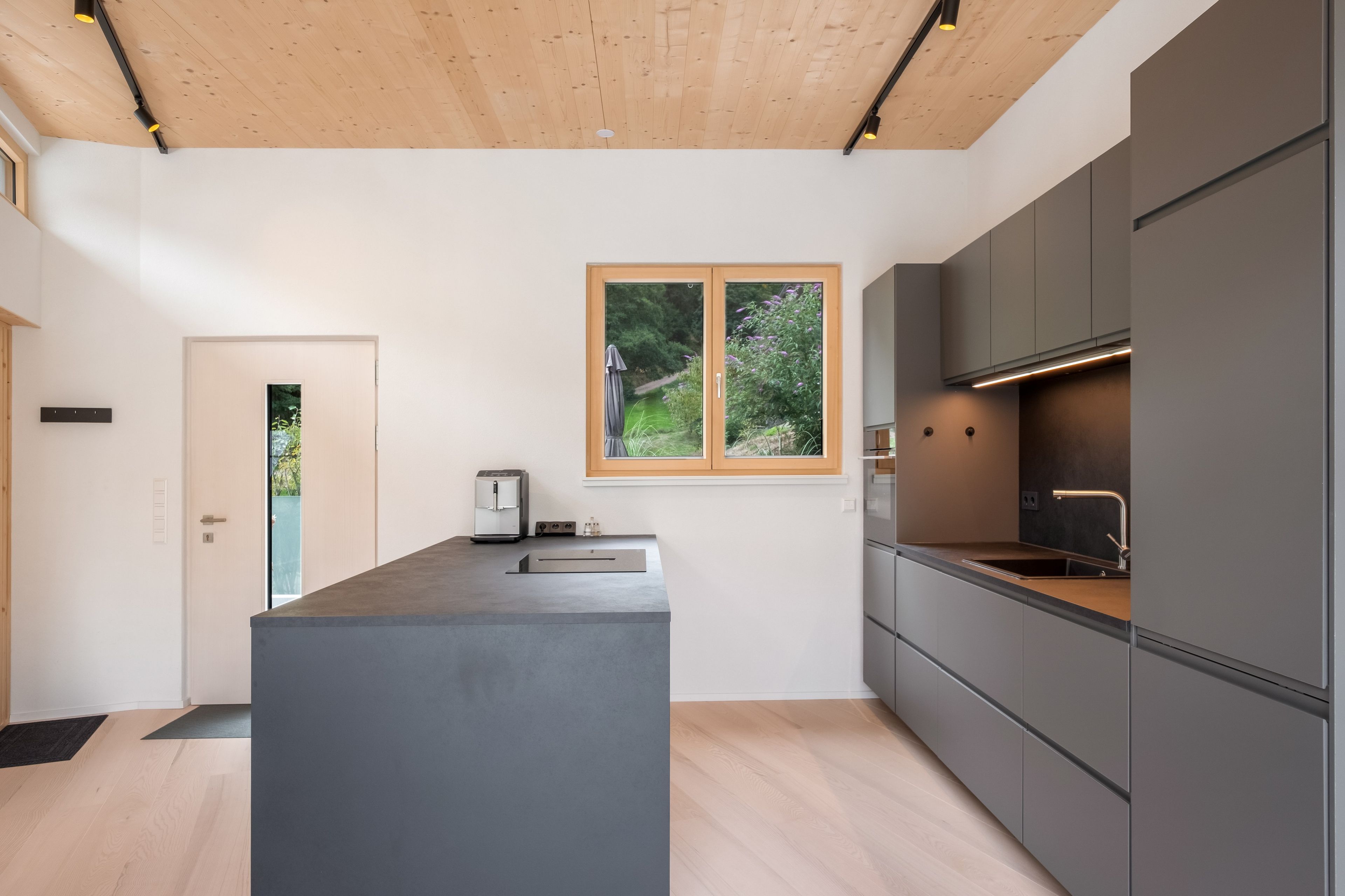 A modern kitchen with a central island, built-in appliances, and a window with a view of greenery.