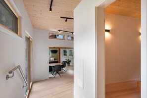 A modern interior with a wooden floor, a dining area with a table and chairs, and a kitchen visible through an open door.
