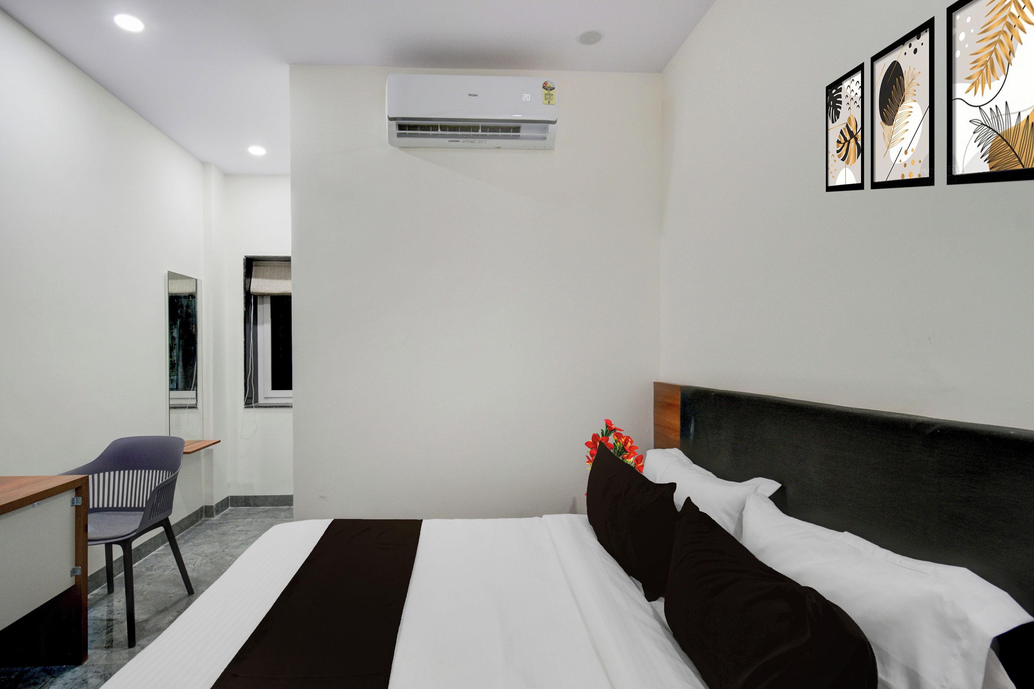 A hotel room with a bed, a desk, a chair, an air conditioner, and framed artwork on the wall.