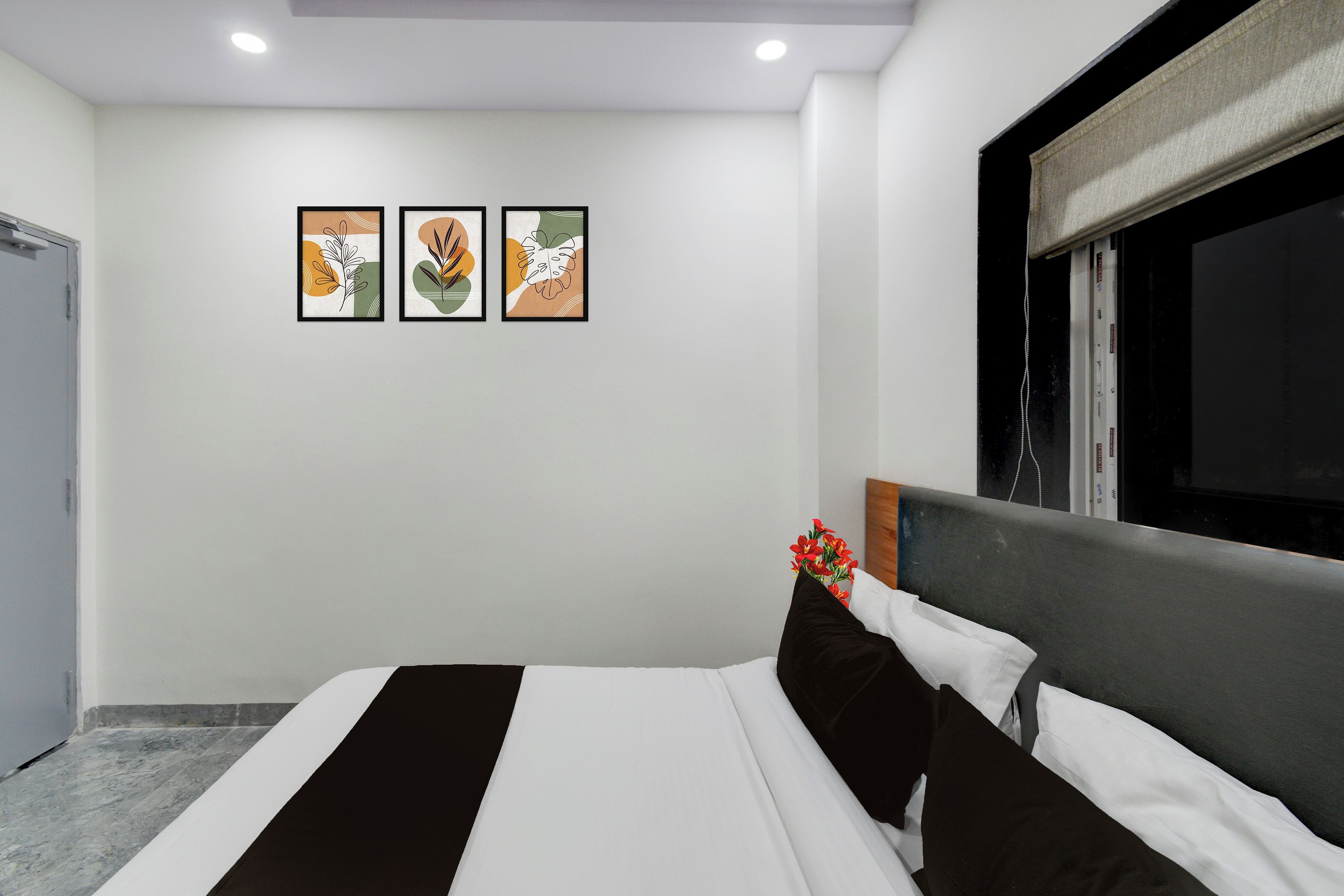 Una habitación de hotel con una cama, un ventanal con cortinas opacas y tres cuadros enmarcados en la pared.