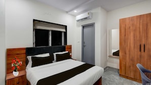 Ein Hotelzimmer mit einem Bett, einem Nachttisch, einem Fenster mit Jalousie, einer Klimaanlage, einem Kleiderschrank und einem Sessel.