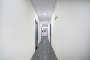 A narrow, well-lit corridor with a tiled floor, white walls, and doors on both sides. - Townhouse Oak L B Nagar Metro Station (Hyderabad)