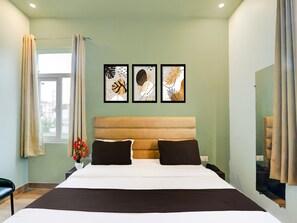 A hotel room with a bed, a window with curtains, and three framed artworks on the wall. - Deluxe Hotel Madhuvan & Lawn (Lucknow)