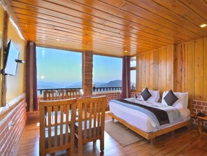 A wooden cabin room with a bed, a TV, and a balcony with a view.
