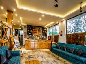 A cozy interior with a wooden bar, a stone wall, and a large window offering a view of trees.