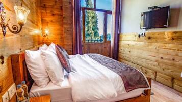 Habitación de madera con una cama, un televisor montado en la pared y una ventana con vistas a árboles.