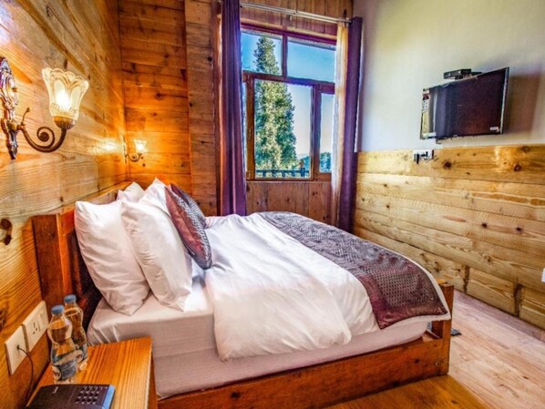 A wooden room with a bed, a TV mounted on the wall, and a window with a view of trees.