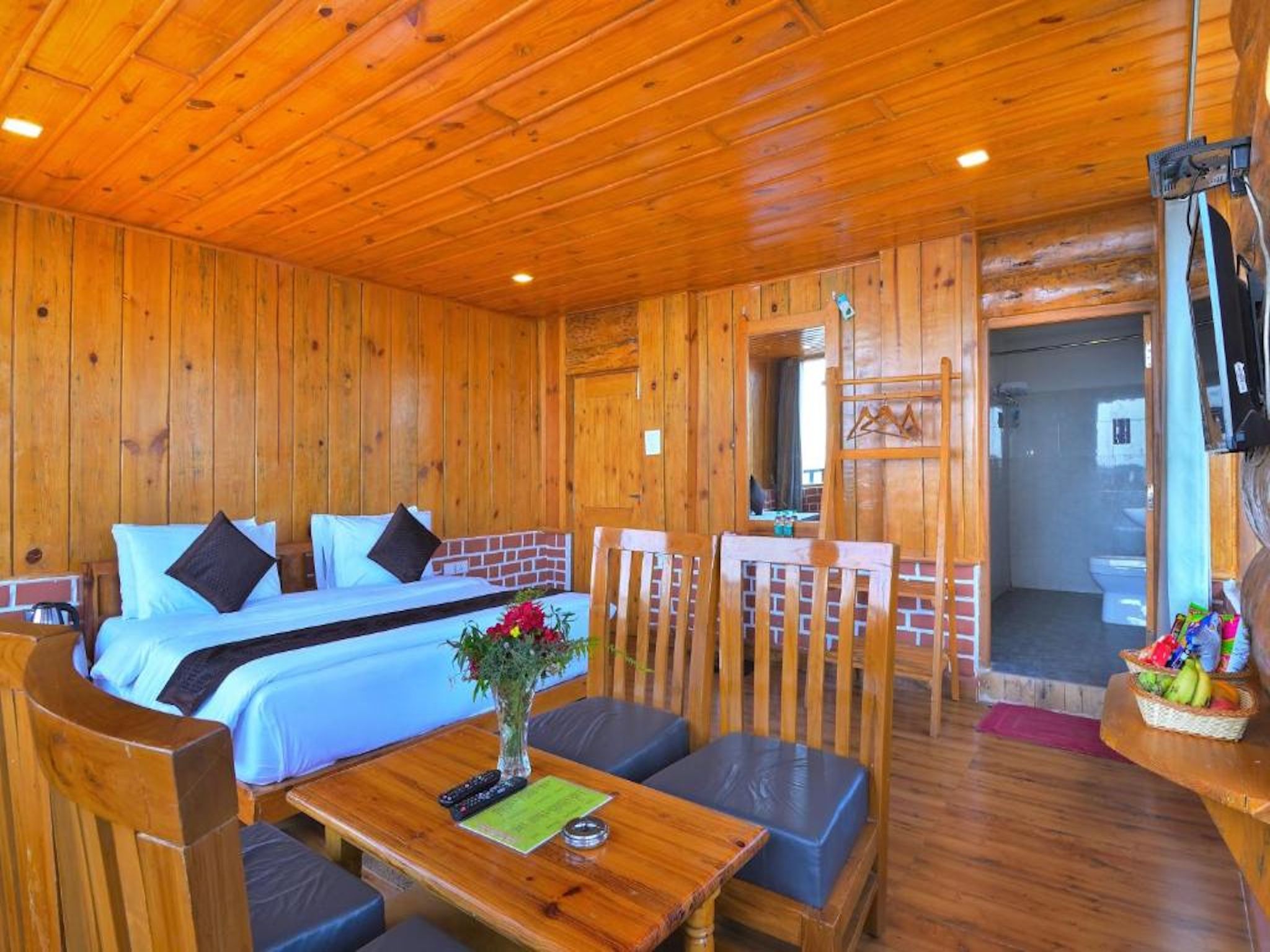 A wooden cabin with a bed, a dining table, and a TV mounted on the wall.