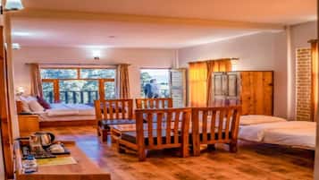 A cozy room with a wooden floor, a bed, a table with chairs, and a window with curtains.