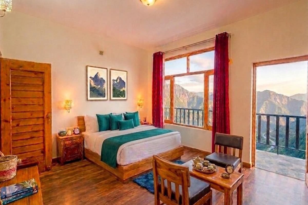 A bedroom with a bed, a chair, a table with tea set, and a window with a mountain view.