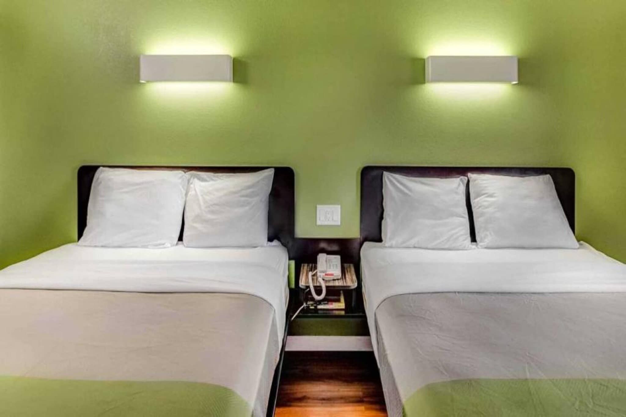 Une chambre double avec deux lits, chacun doté de draps blancs, une table de chevet avec un téléphone et des murs verts.