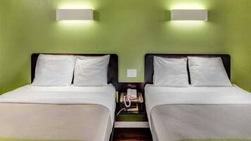 Une chambre double avec deux lits, chacun doté de draps blancs, une table de chevet avec un téléphone et des murs verts.