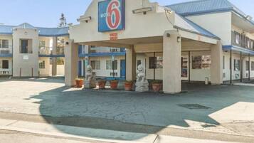 Un motel avec une grande enseigne indiquant « Motel 6 » et un espace de stationnement couvert agrémenté de plantes en pot.