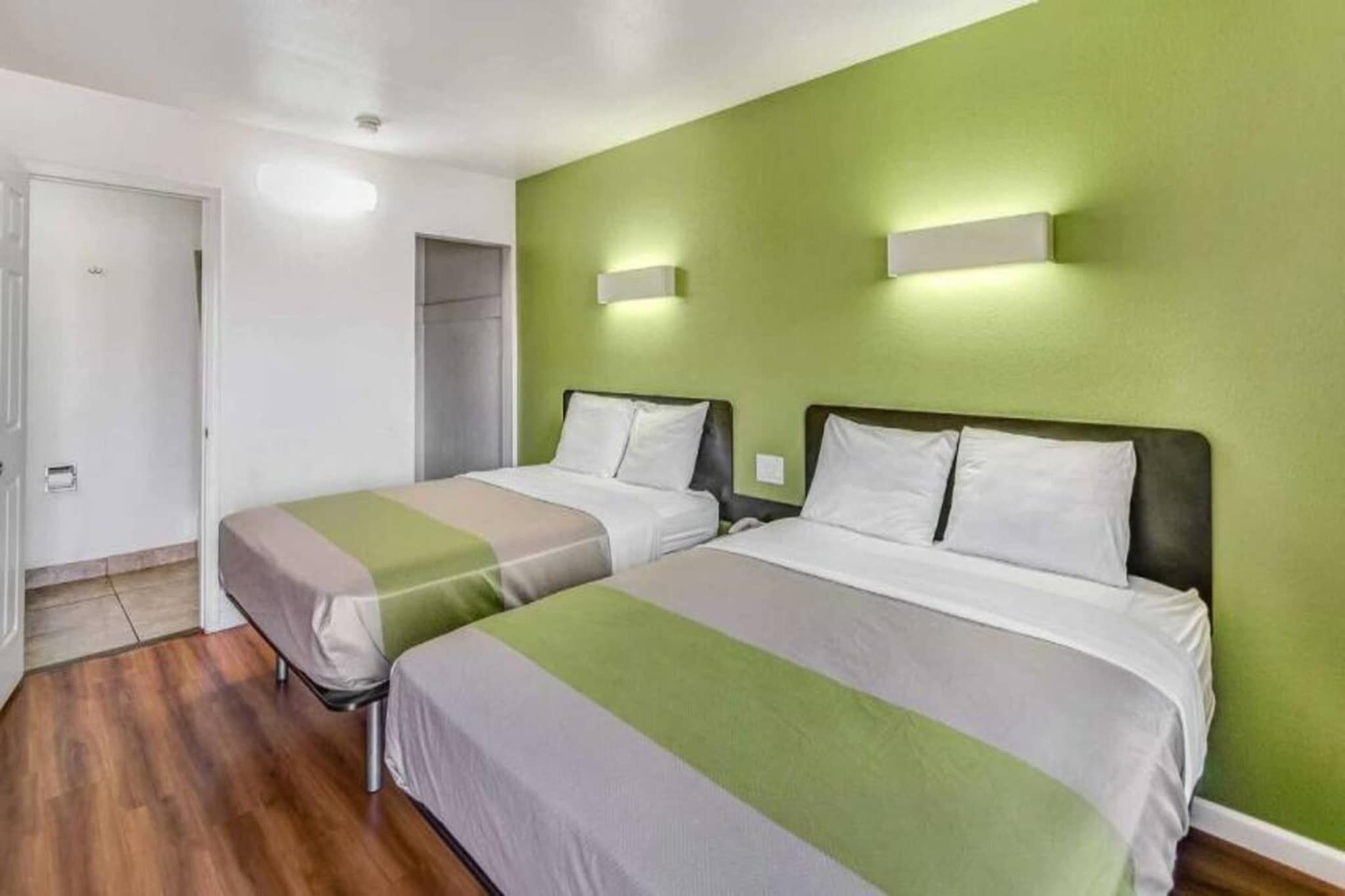 Quarto de hotel com duas camas, parede verde e piso de madeira.