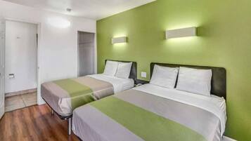 Quarto de hotel com duas camas, parede verde e piso de madeira.