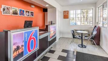 Un espace d’accueil d’hôtel comprenant un comptoir d’enregistrement, un coin salon avec une table et des chaises, et une fenêtre donnant sur l’extérieur.