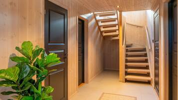 Un couloir intérieur en bois, agrémenté d’une plante en pot, d’un escalier et d’une porte.