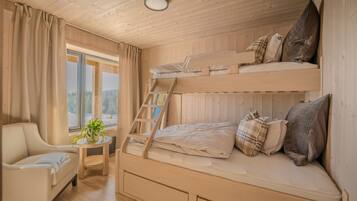Una habitación de cabaña acogedora con una cama litera, una silla, una mesita con una planta y una ventana con vistas a árboles.