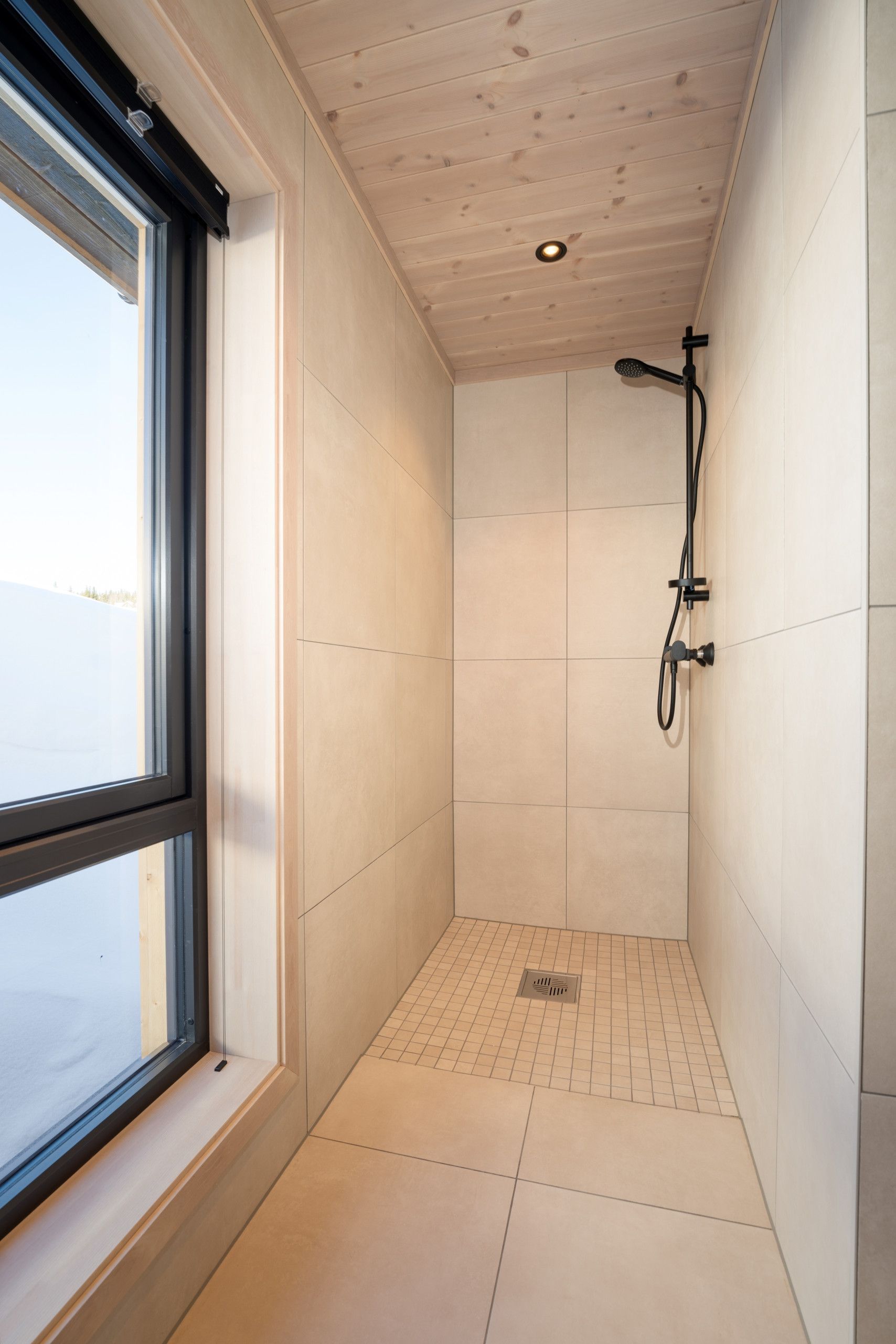 Une petite salle de douche moderne, dotée d’une fenêtre, de murs carrelés et d’un pommeau de douche apparent.