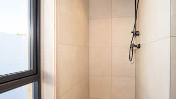 Une petite salle de douche moderne, dotée d’une fenêtre, de murs carrelés et d’un pommeau de douche apparent.