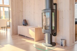 A modern interior with a wood-paneled wall, a glass-top table, and a built-in wood stove. - Spacious and modern cabin in Skeikampen (Gudbrandsdalen)
