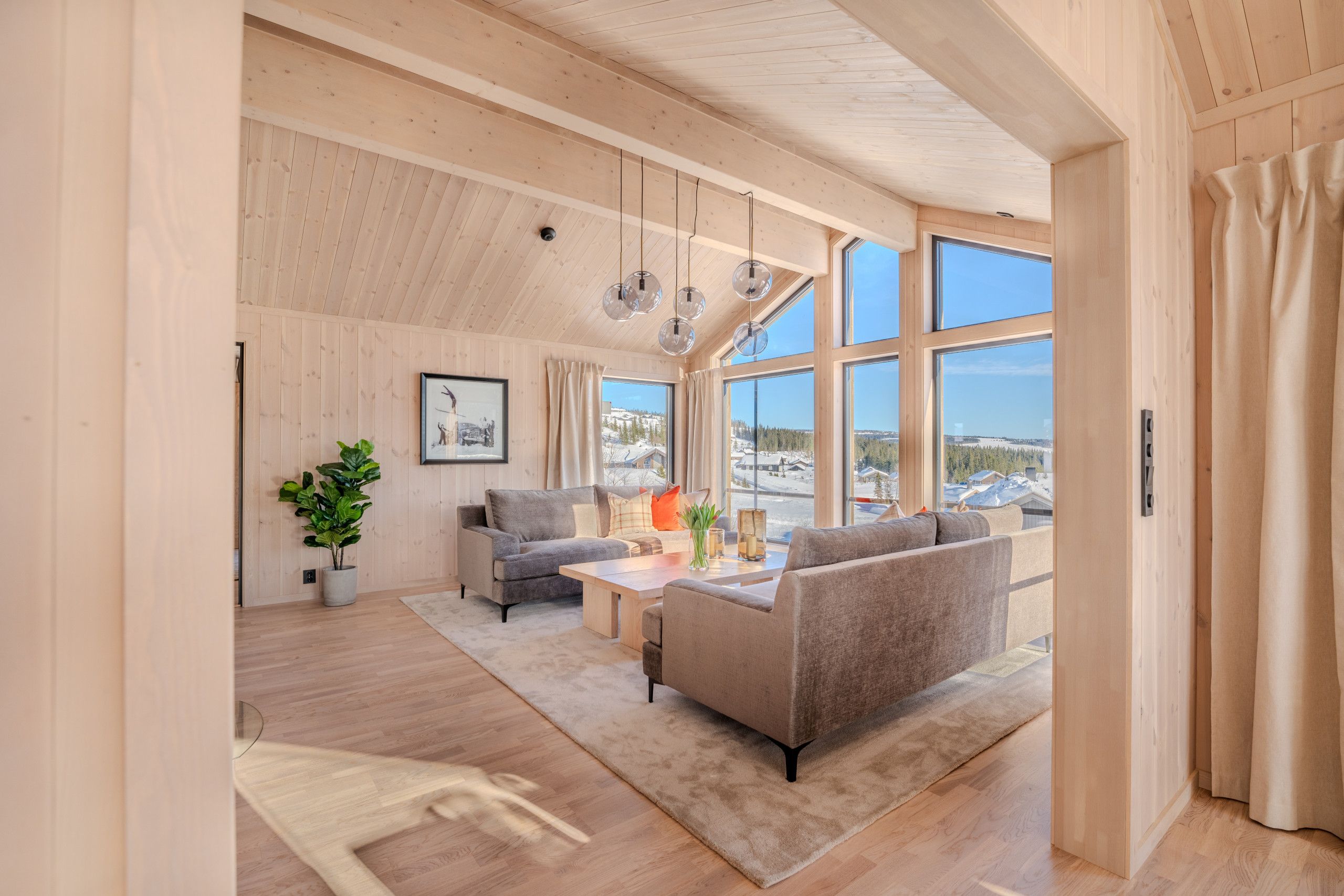 Un vaste espace de vie doté d’un plafond haut, de murs en bois et de grandes fenêtres offrant une vue sur un paysage enneigé.