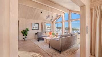 Un vaste espace de vie doté d’un plafond haut, de murs en bois et de grandes fenêtres offrant une vue sur un paysage enneigé.