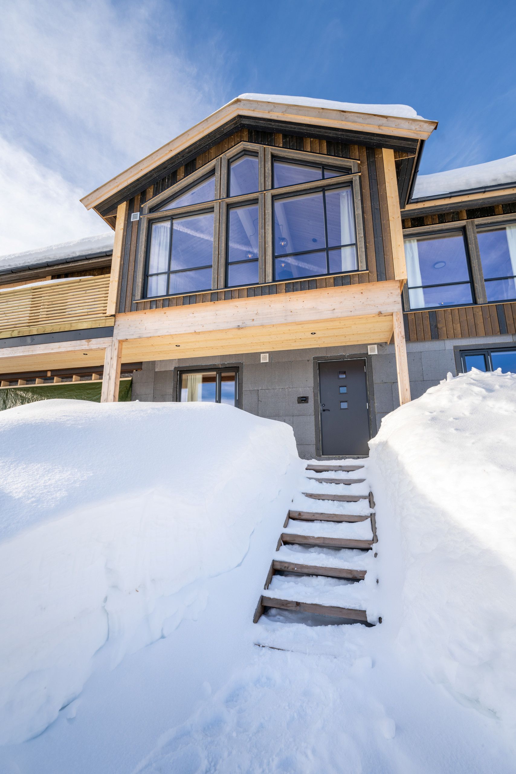 Un bâtiment moderne avec une façade en bois, de grandes fenêtres et une entrée recouverte de neige.