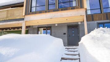 Un bâtiment moderne avec une façade en bois, de grandes fenêtres et une entrée recouverte de neige.