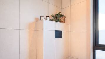 Un baño moderno con inodoro blanco, un ventanal pequeño y un estante en la pared con artículos de aseo.