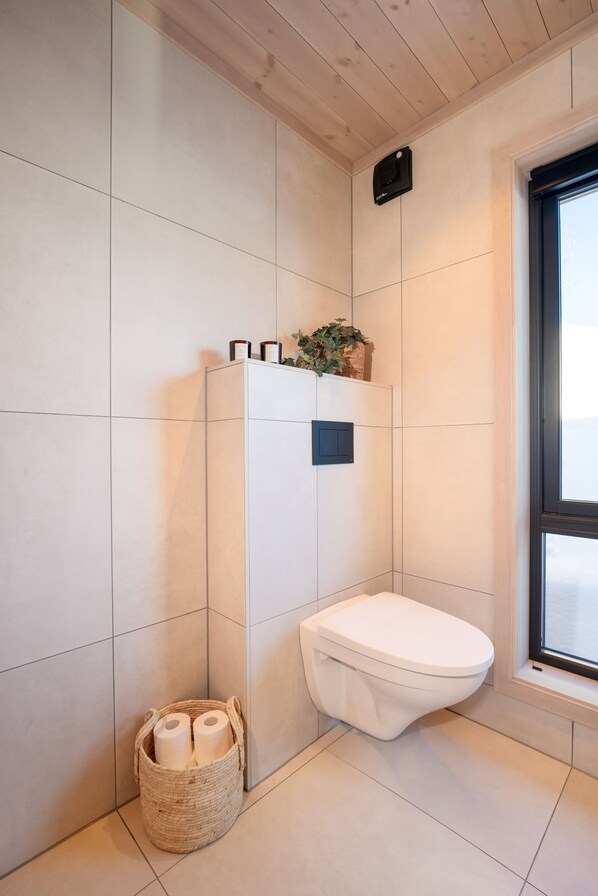 A modern bathroom with a white toilet, a small window, and a wall-mounted shelf with toiletries.
