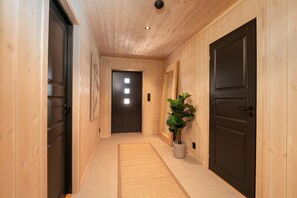 A hallway with wooden walls, a dark door at the end, and a potted plant. - Spacious and modern cabin in Skeikampen (Gudbrandsdalen)