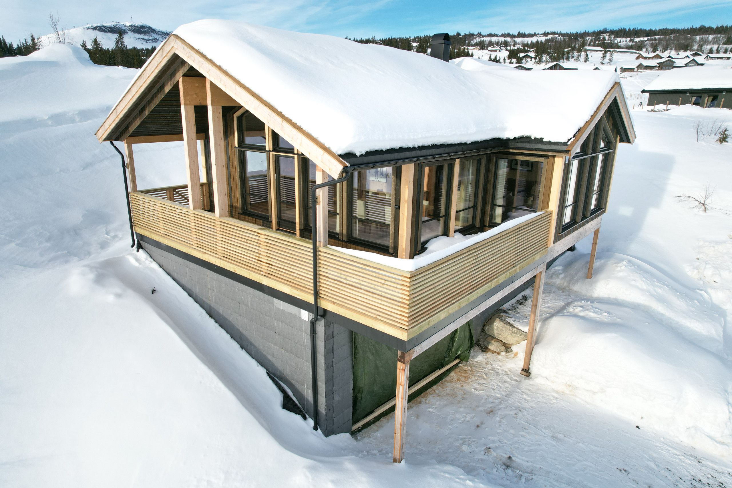 Una cabaña de madera cubierta de nieve con ventanas grandes y un balcón.