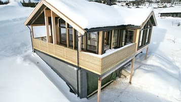 Una cabaña de madera cubierta de nieve con ventanas grandes y un balcón.